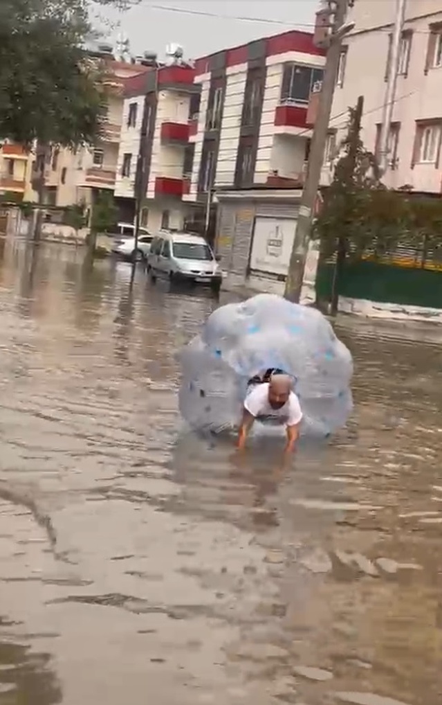 Mersin Tarsus'ta sağanakla göle dönen caddede bir kişi şişme şeffaf balonla ilerledi